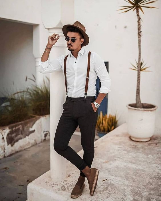 Handsome brunette man with a beard in a white shirt vest and black pants  sits on